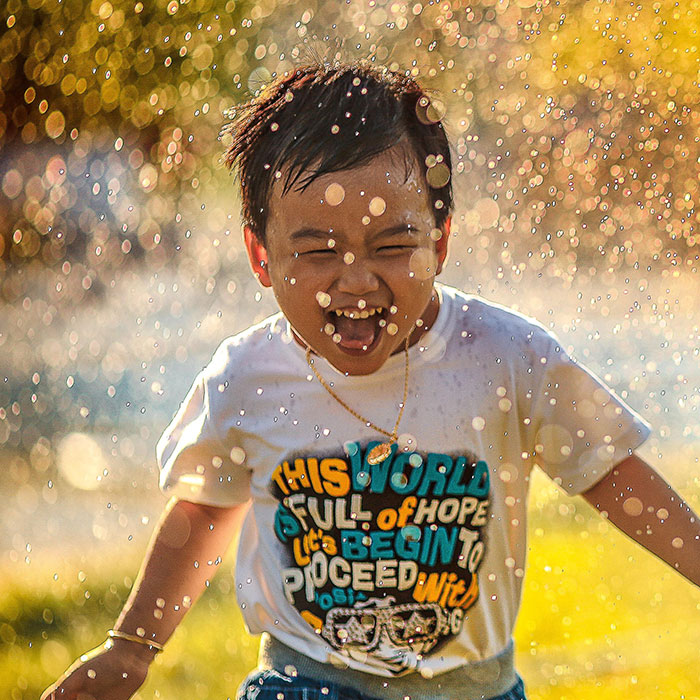 Young boy running through sprinkler, smiling | SungateKids | Child Abuse Awareness, Support & Advocacy